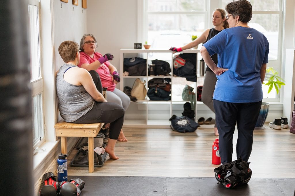 A group of body-neutral women in a room talking to each other at a women's-only gym.
