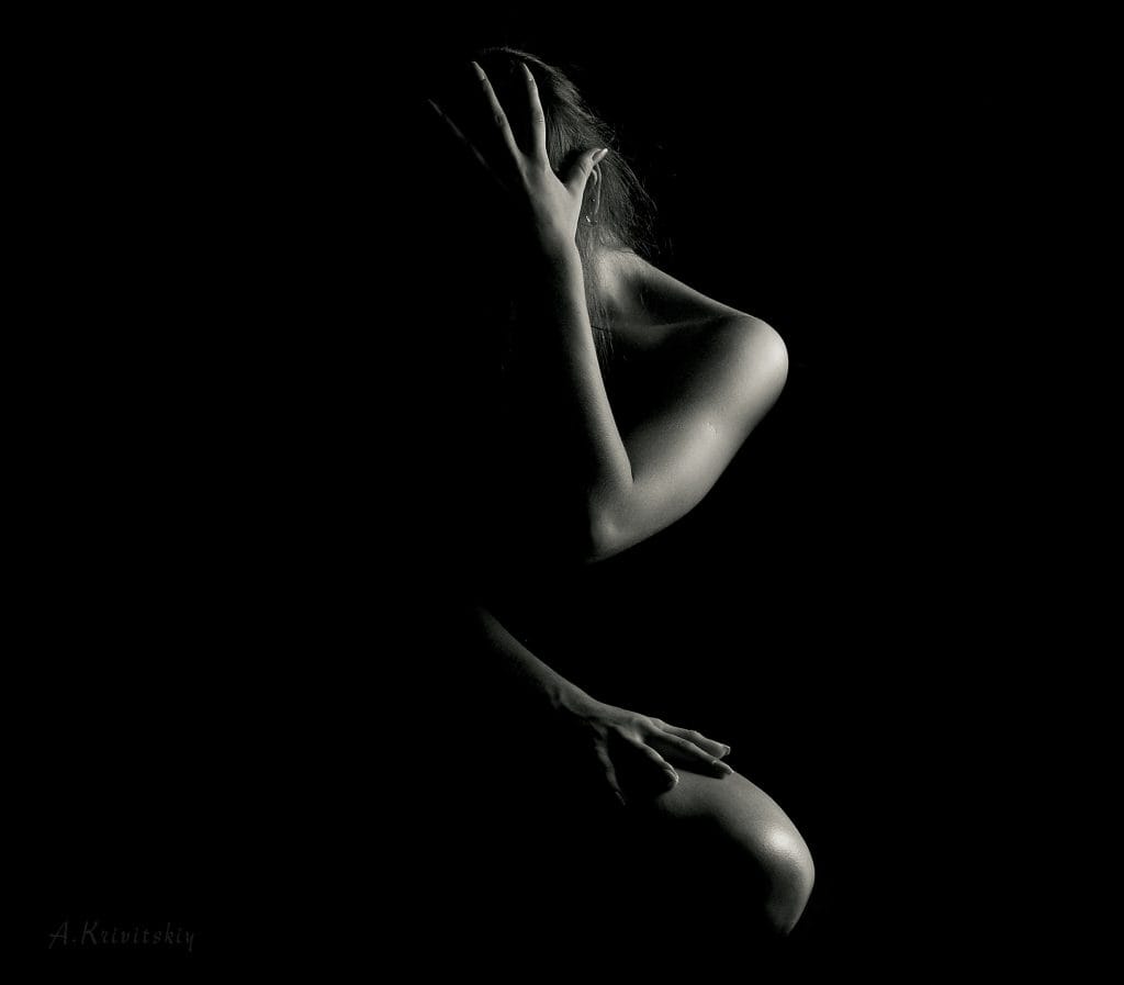 A body-neutral photo of a fitness woman posing in the dark.